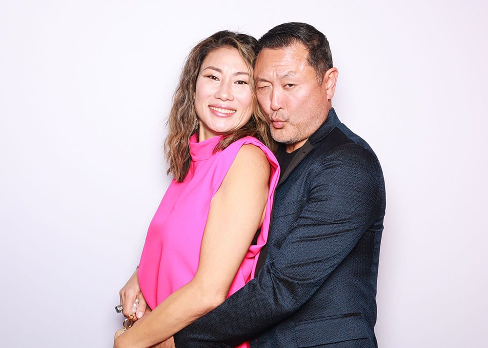 Couple posing playfully in a photo booth, woman in a pink top and man in a dark blazer, showcasing a fun and romantic photo booth pose.