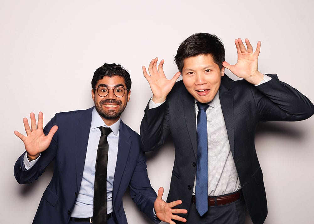 Two men in suits making playful "scared" expressions with hands raised, embodying a fun photo booth pose.