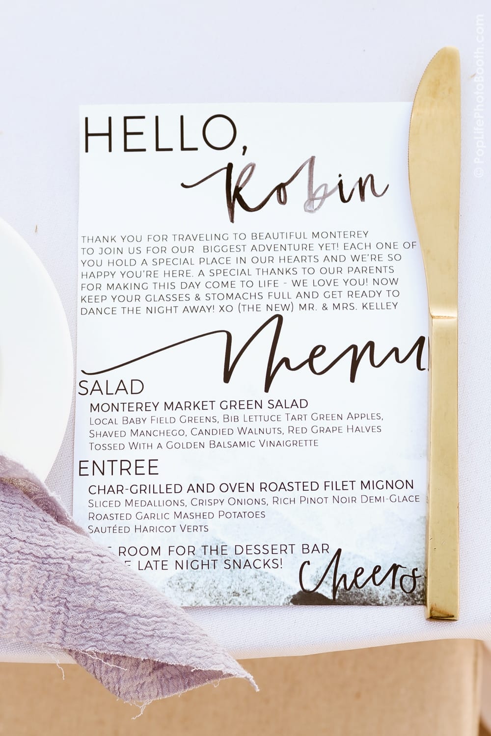 Menu card for wedding reception featuring a personalized greeting, detailed food offerings including salad and entrée options, and a note about dessert and late-night snacks, placed on a table setting with a gold knife and lavender napkin.