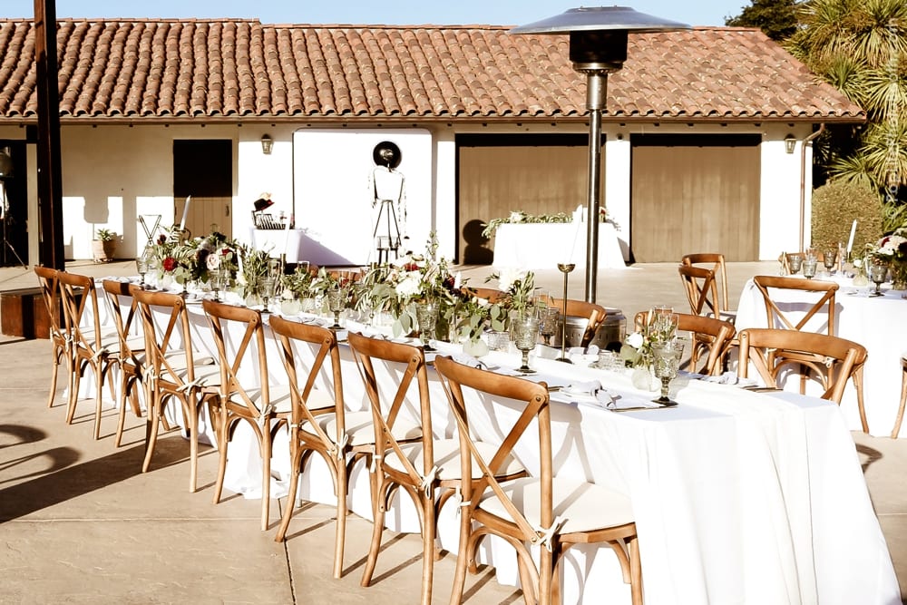 Elegant wedding reception setup with long wooden tables adorned with floral centerpieces and glassware, featuring a photo booth in the background, capturing the joyful atmosphere of Thomas and Anastasha's special day.
