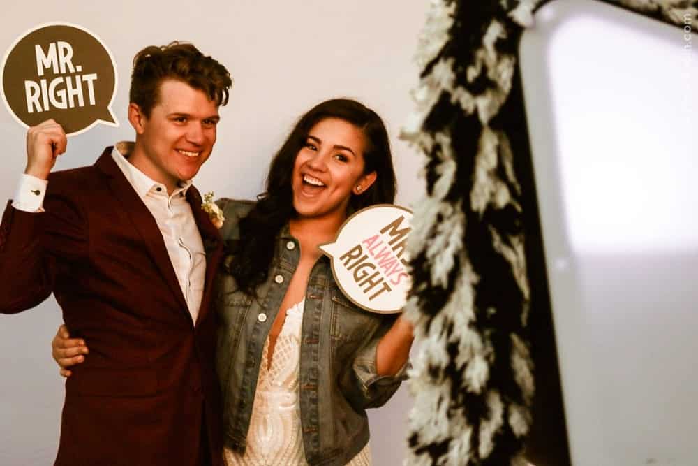 Couple posing in photo booth with playful signs reading "MR. RIGHT" and "MRS. ALWAYS RIGHT," capturing joyful wedding moment at Thomas and Anastasha's celebration.