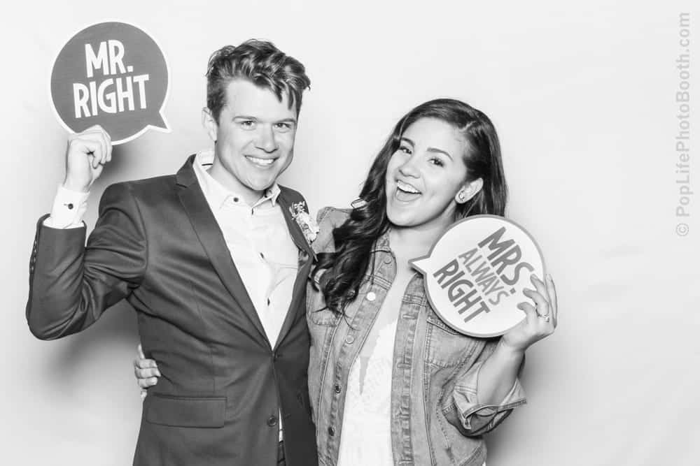 Couple posing in photo booth, holding signs "MR. RIGHT" and "MRS. ALWAYS RIGHT," showcasing fun and playful moments from Thomas and Anastasha's wedding celebration.