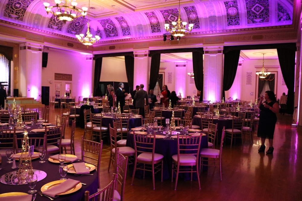 Elegant event space with purple lighting, decorated tables, and attendees mingling, showcasing a gala atmosphere suitable for celebrations and event planning.