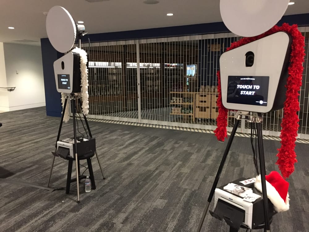 Photo booth setup with two booths displaying "Touch to Start" prompts, decorated with festive garlands, in a venue setting, illustrating event planning and photo booth rental services.