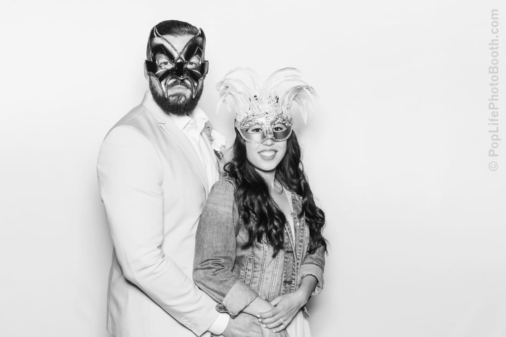Couple posing in masquerade masks against a white backdrop, showcasing holiday glam for a festive photo booth experience.