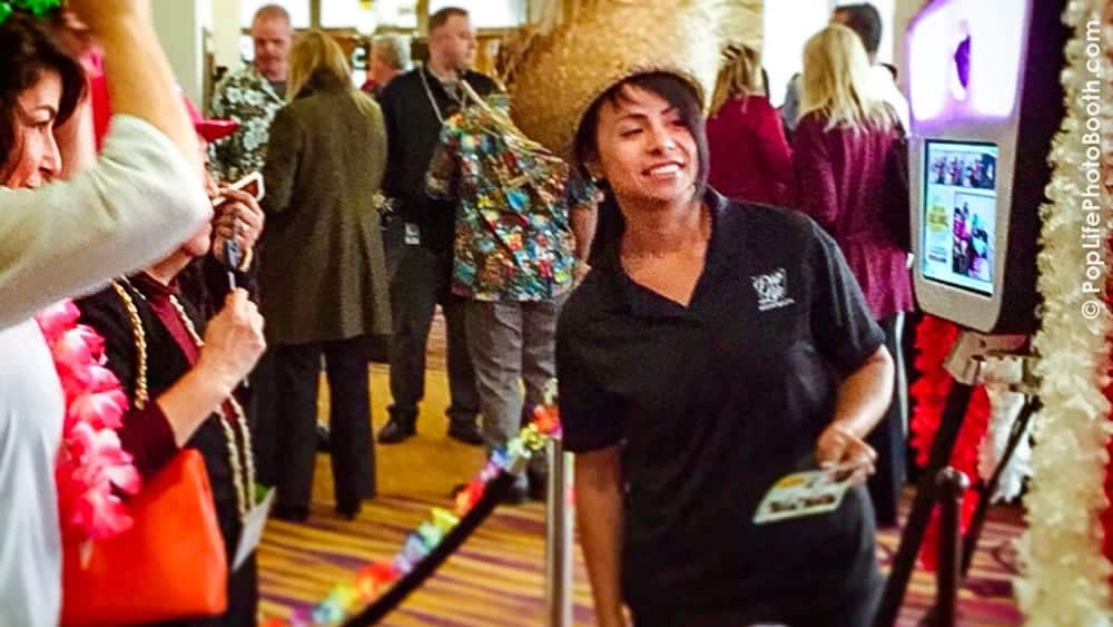 Guests enjoying a casino-themed party with a photo booth, woman wearing a straw hat, colorful leis, and festive decorations in the background.