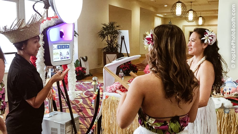 Photo booth setup featuring a staff member in a straw hat interacting with guests in tropical attire, capturing memories at a casino-themed party with vibrant decorations.