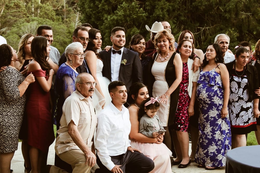 Group of wedding guests posing together, celebrating the couple's special day, showcasing joy and familial connections in an outdoor setting.