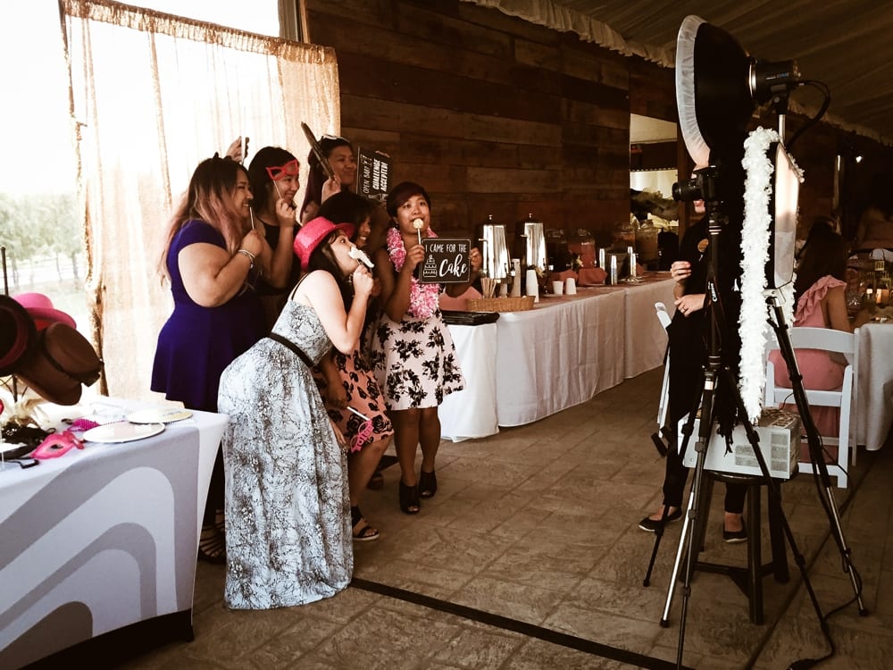 Group of women posing with props in front of a photo booth at a wedding reception, celebrating and enjoying the event atmosphere.