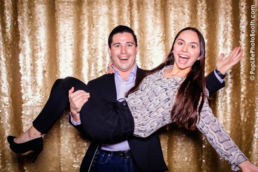 Guests enjoying a fun moment in a photo booth at a Thanksgiving corporate event, with a shiny gold backdrop and playful expressions, showcasing Pop Life Photo's services.