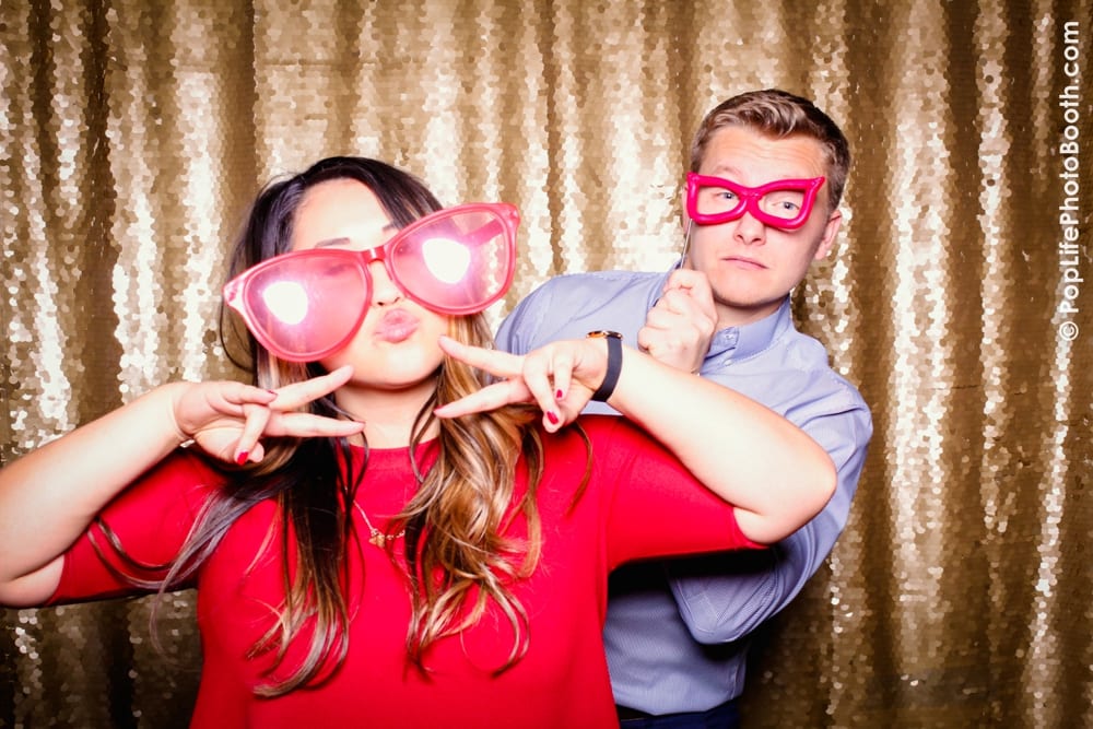 Guests at a Thanksgiving event posing playfully in a photo booth, wearing oversized pink glasses, with a sparkling gold backdrop.
