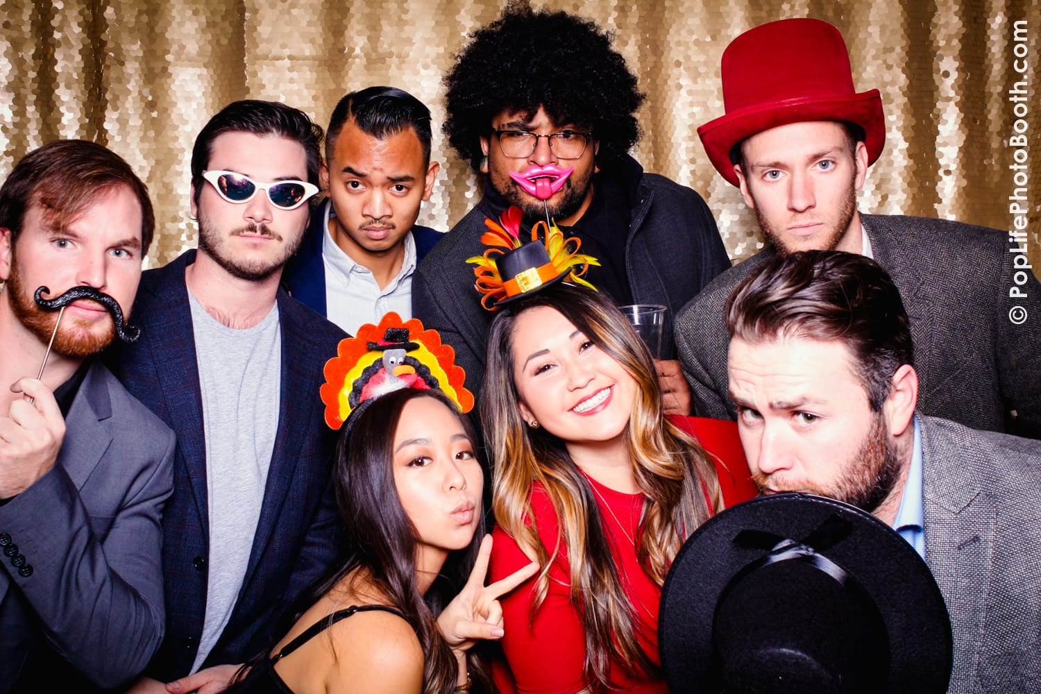 Group of friends posing with fun props, including hats and mustaches, in a festive photo booth setting, capturing the lively atmosphere of the Yelpsgiving event at Yelp's corporate office in San Francisco.