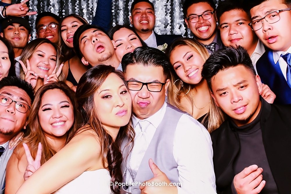 Newlywed couple posing with friends in a lively photo booth setting at Casa Real, Livermore, featuring a silver sequins backdrop.