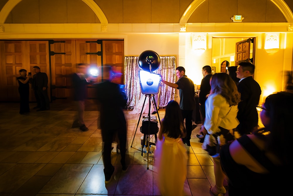 Attendant assisting guests with Studio Retro Photo Booth at Casa Real, vibrant event atmosphere with golden lighting and elegant decor.