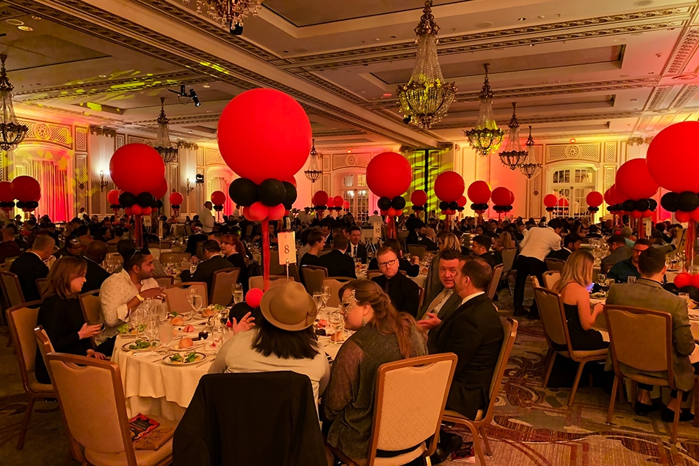 Elegant ballroom event at the Palace Hotel in San Francisco, featuring guests dining at tables adorned with red and black balloon centerpieces, chandeliers, and sophisticated décor.