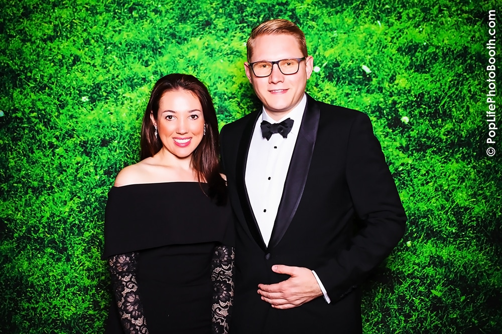 Couple posing in formal attire against a vibrant green moss backdrop at The Olympic Club, showcasing Pop Life Photo Booth's event photography services.