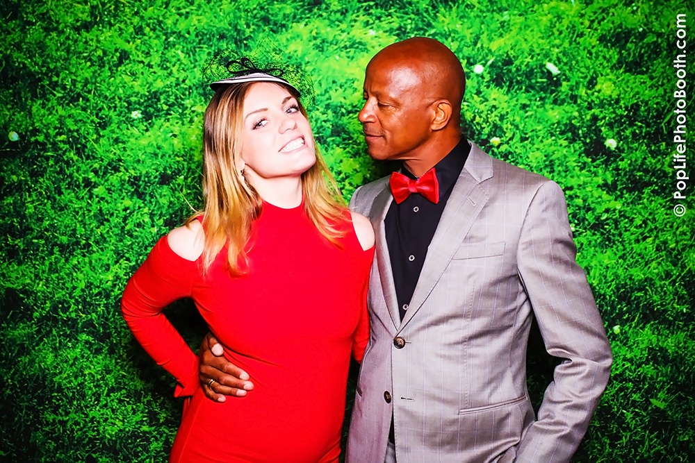 Couple posing playfully in a photo booth with a vibrant green moss backdrop, showcasing a fun atmosphere ideal for weddings and events in San Francisco.