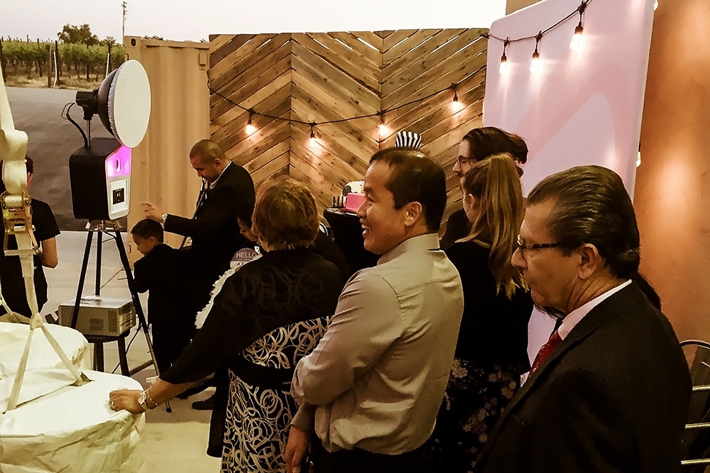 Guests waiting in line at a photo booth station inside McGrail Vineyard, featuring a wooden backdrop, string lights, and event setup, capturing the lively atmosphere of a gathering in Livermore Valley Wine Country.