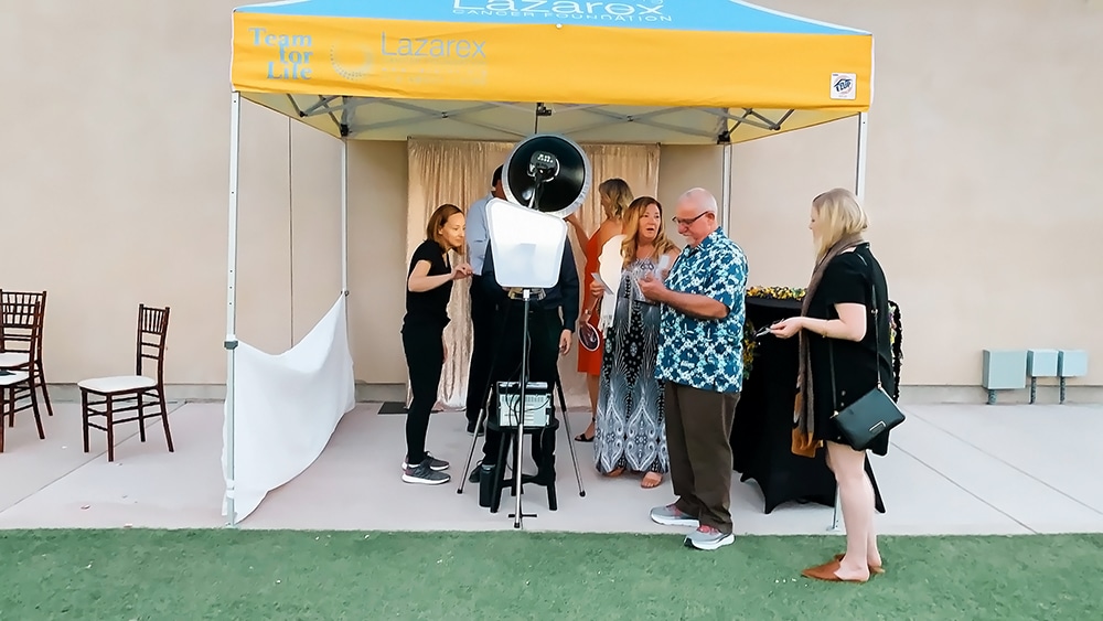 People interacting at a photo booth station under a yellow Lazarex Foundation tent during a Lazerex Cancer Fundraiser at Garré Vineyard & Winery in Livermore, California.