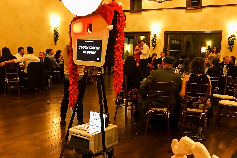 Photo booth setup with touch screen display and festive decorations, surrounded by guests enjoying a wedding reception at Las Positas Vineyards.