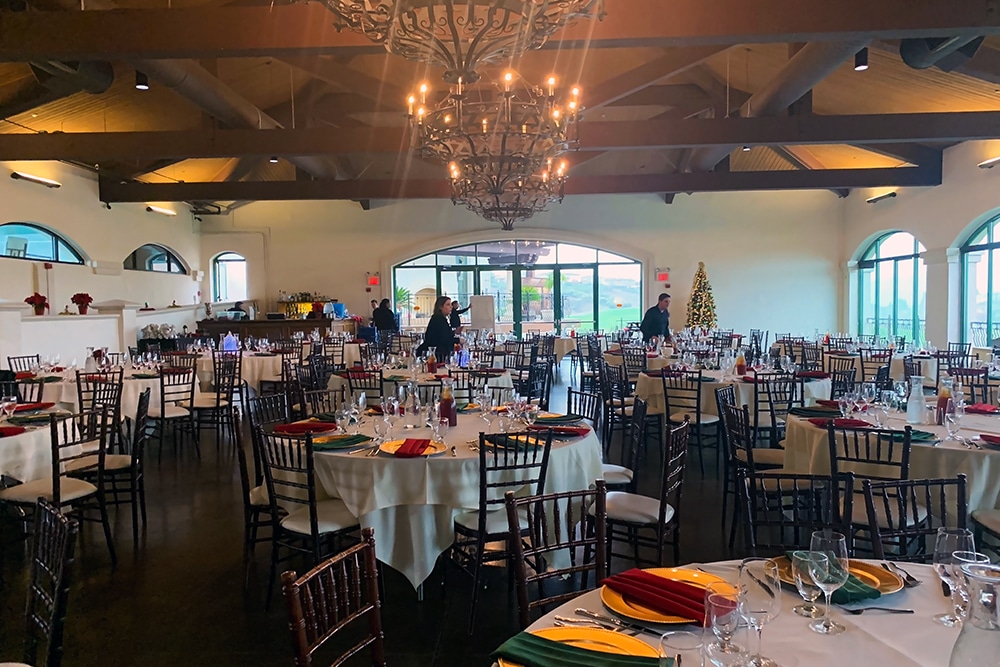 Elegant ballroom setup at Bridges Golf Club in San Ramon, featuring round tables with colorful table settings, a chandelier, and large windows overlooking lush greenery, ideal for weddings and events.
