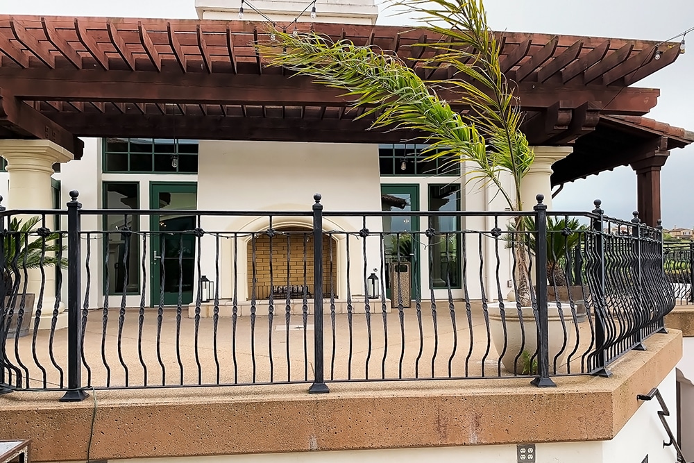 Patio area with wrought-iron railing and Mediterranean-style architecture at Bridges Golf Club, featuring a fireplace and lush landscaping, ideal for events and gatherings.