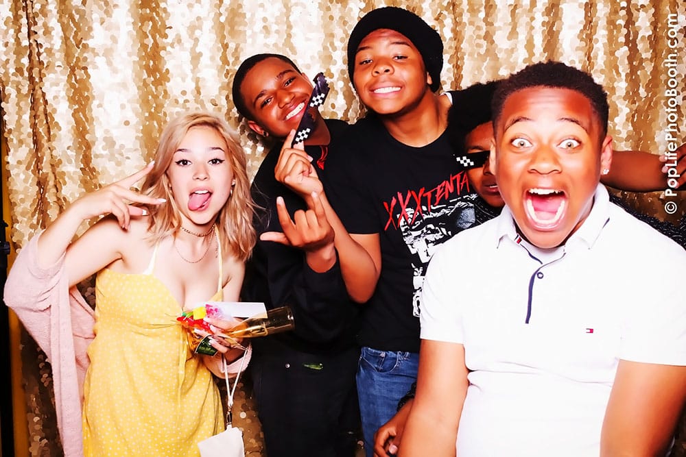 Students enjoying a fun moment in a photo booth at a school dance, with playful expressions and props, capturing the excitement of the event.
