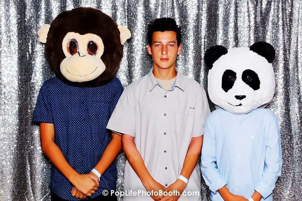 Students wearing fun animal masks, including a monkey and a panda, posing together in front of a sparkling backdrop at a school event photo booth.