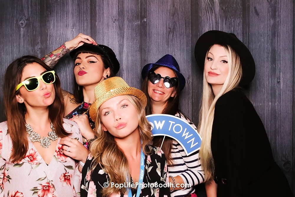 Group of women posing playfully in a photo booth with props, wearing sunglasses and hats, at the Roundhouse in San Ramon during a corporate event for Social Survey.