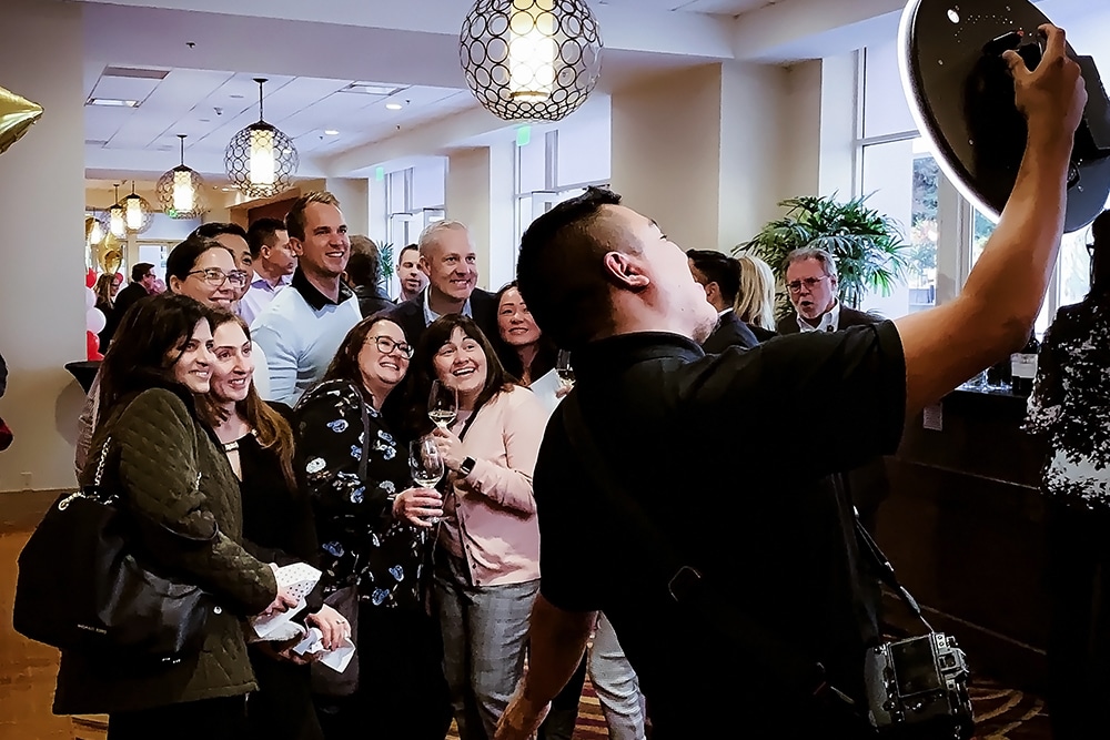 Group of smiling guests posing for a photo at the San Ramon Marriott corporate event, with a photo booth operator capturing the moment.