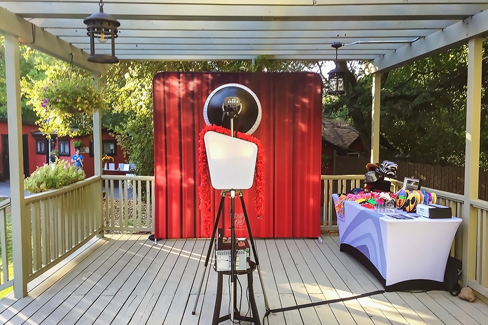 Photo booth setup in gazebo at The Ranch at Little Hills, featuring a red curtain backdrop, lighting equipment, and a table with colorful props for guests.