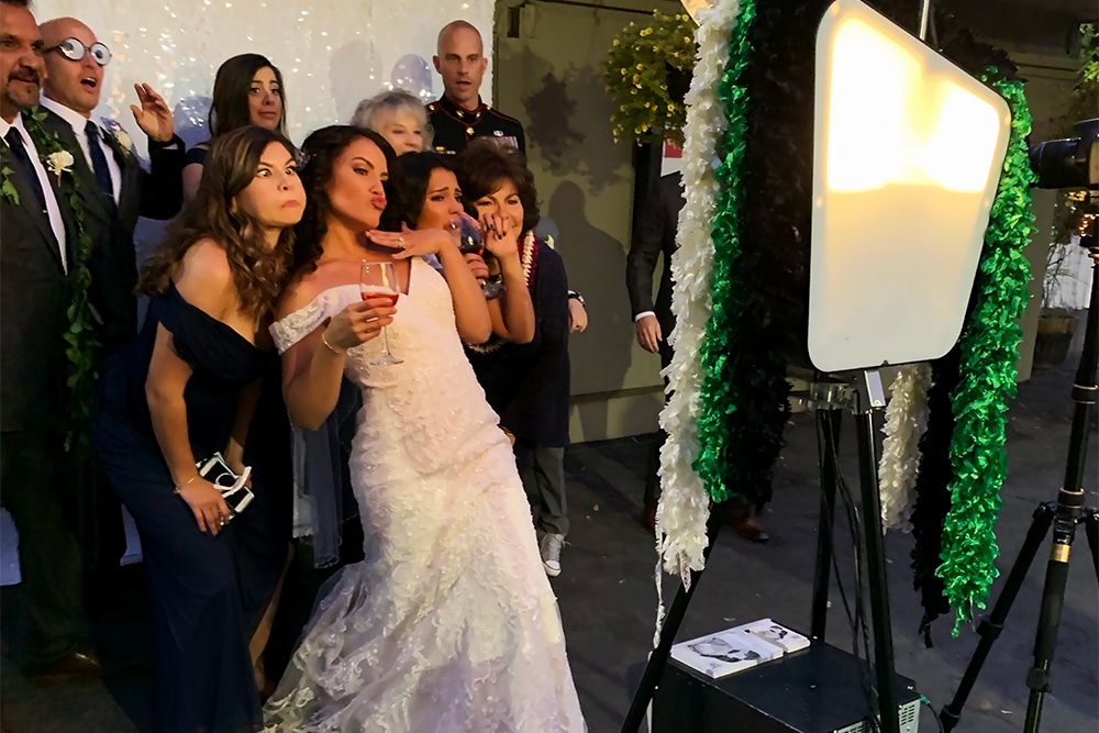Wedding guests posing playfully at a photo booth during a celebration at The Ranch at Little Hills, featuring a bride in a lace gown and festive decorations.