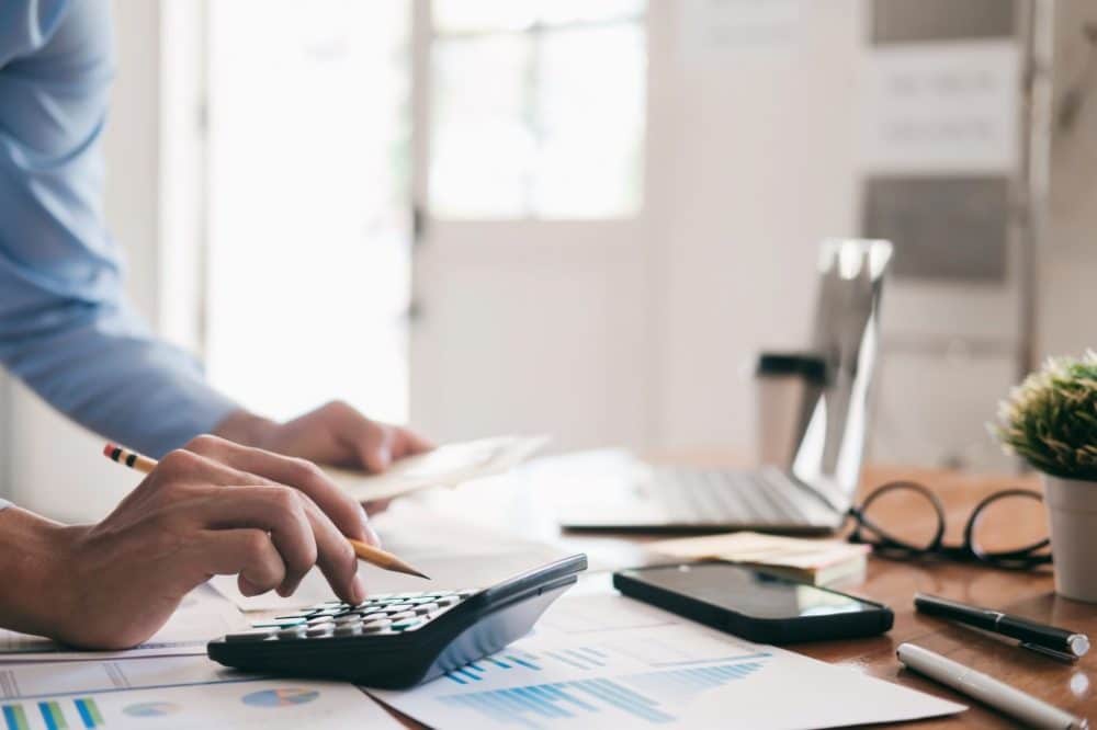 Person calculating budget with calculator and documents on desk, emphasizing financial planning for holiday party organization.