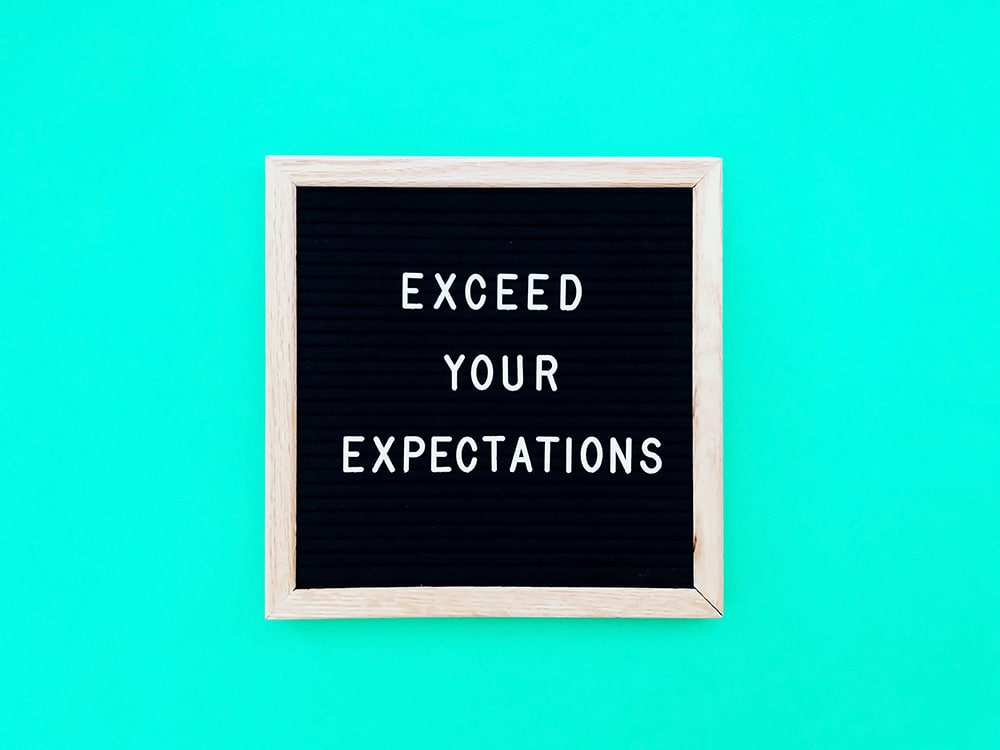"Black letter board with the motivational phrase 'Exceed Your Expectations' on a teal background, emphasizing goal-setting and managing expectations in last-minute event planning."