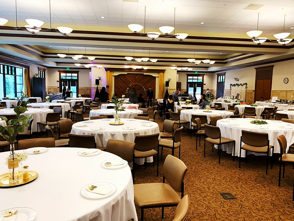 Event venue setup with round tables, white tablecloths, and centerpieces, illustrating a well-organized space for a gathering, emphasizing crowd management and health safety for post-Covid-19 events.