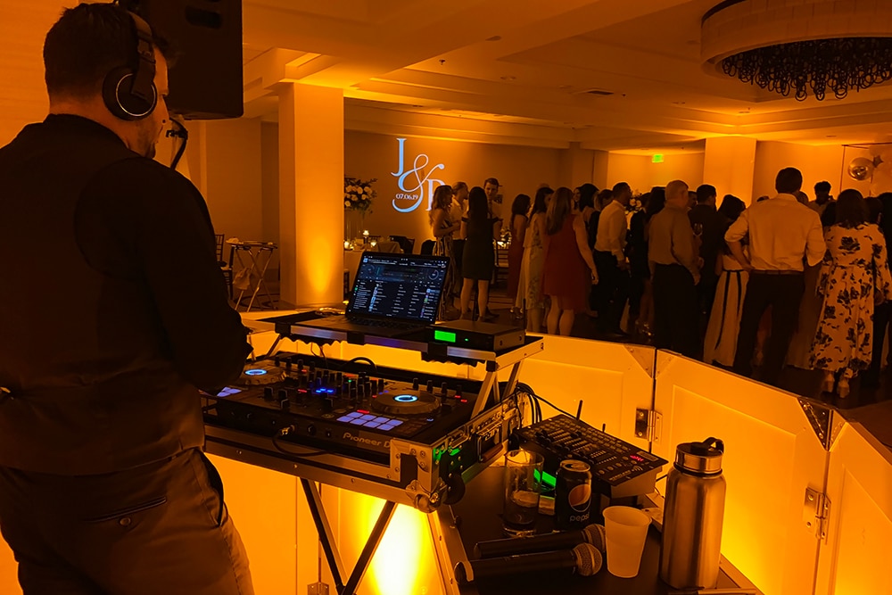 DJ performing at San Ramon Marriott event, illuminated by warm lighting, with guests dancing in the background, showcasing a lively atmosphere for corporate and private events.