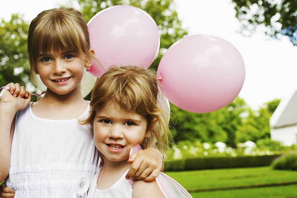 Happy girls in white dresses holding pink balloons at a wedding, capturing joyful moments and fun experiences.