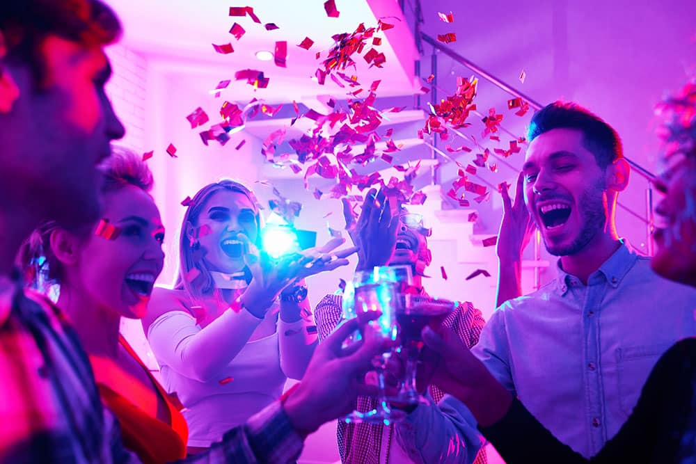 Group of joyful people celebrating at a corporate party, raising glasses and surrounded by colorful confetti under vibrant lighting.