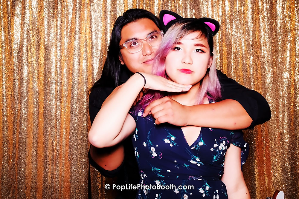 Couple posing playfully in a photo booth with a glittering backdrop, showcasing fun moments from a wedding celebration.