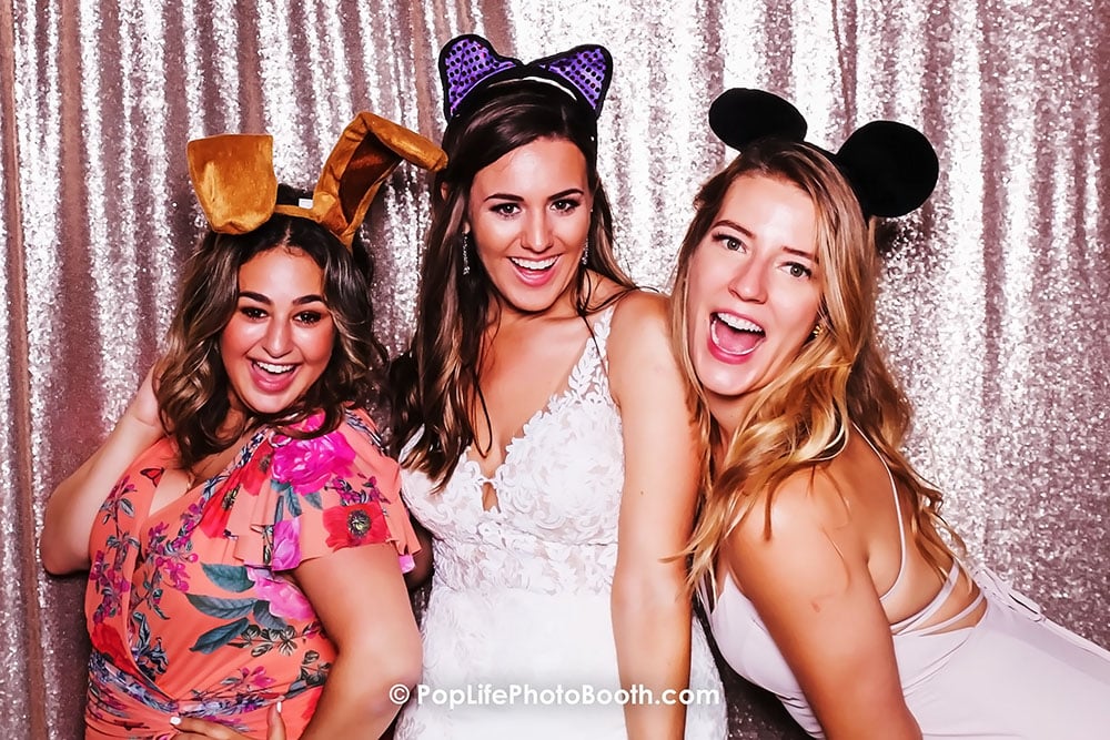 Happy bride and friends wearing fun hats in photo booth, celebrating wedding memories at Terra Gallery, San Francisco.