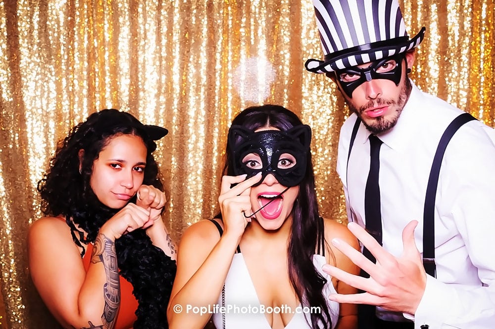 Friends enjoying a fun photo booth experience, wearing playful masks and costumes, with a sparkling gold backdrop, perfect for enhancing wedding celebrations.