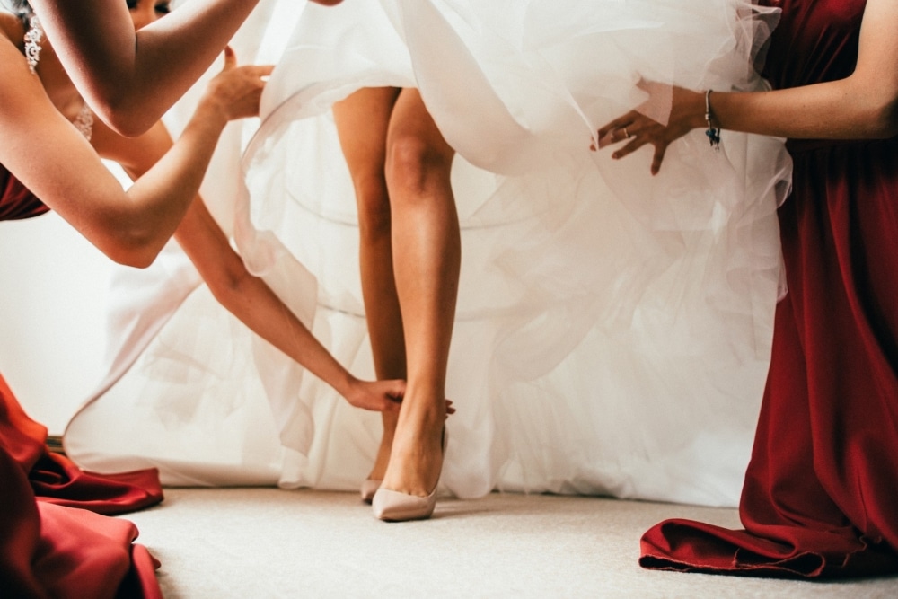 Bride adjusting wedding dress with assistance from bridesmaids, emphasizing comfort and movement during dress fitting.