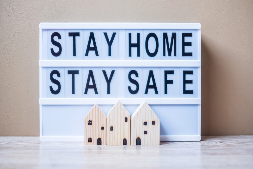 Lightbox sign displaying "STAY HOME STAY SAFE" with wooden house decorations, emphasizing safety measures for events during the COVID-19 pandemic.