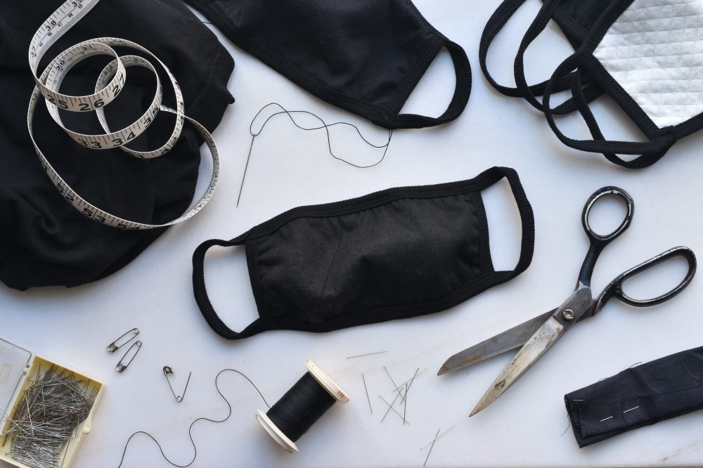 Homemade black face masks, sewing tools including scissors, measuring tape, thread, and pins, promoting safety and hygiene at events.