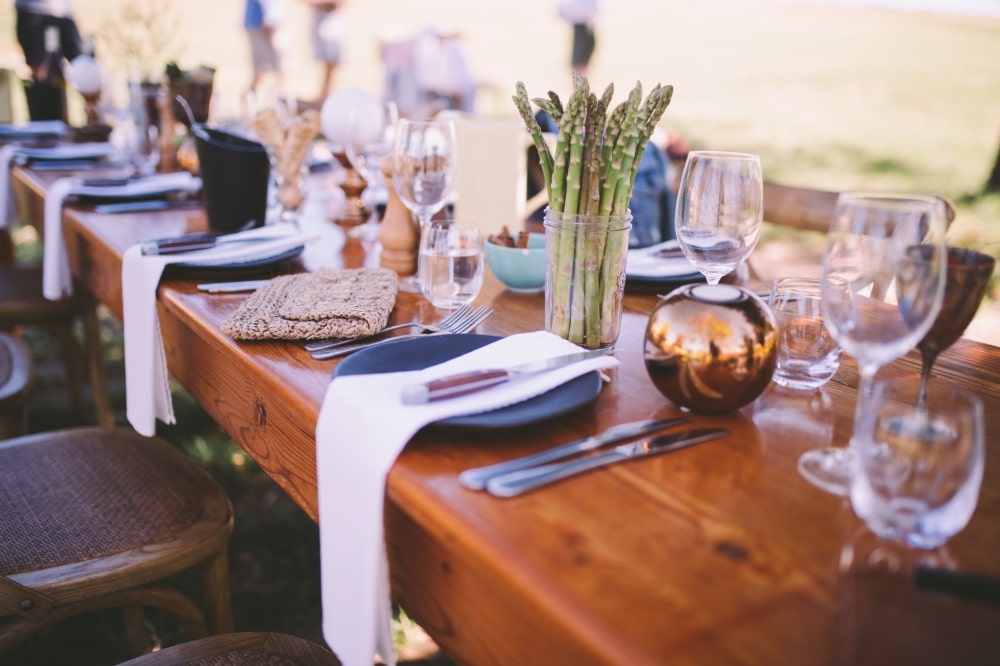Elegant dining table set for an event, featuring cutlery, wine glasses, and a centerpiece of asparagus, emphasizing a festive atmosphere for weddings or receptions.