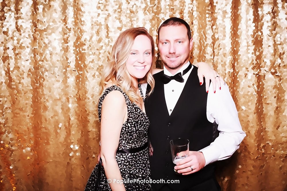 Couple posing happily in front of a shimmering gold backdrop, showcasing a fun and festive atmosphere, ideal for event photography and photo booth experiences.