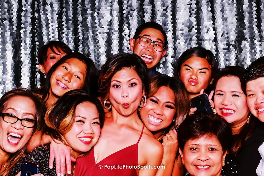 Cheerful group of friends posing in a photo booth with a sparkling backdrop, showcasing fun and memorable moments at a wedding celebration.