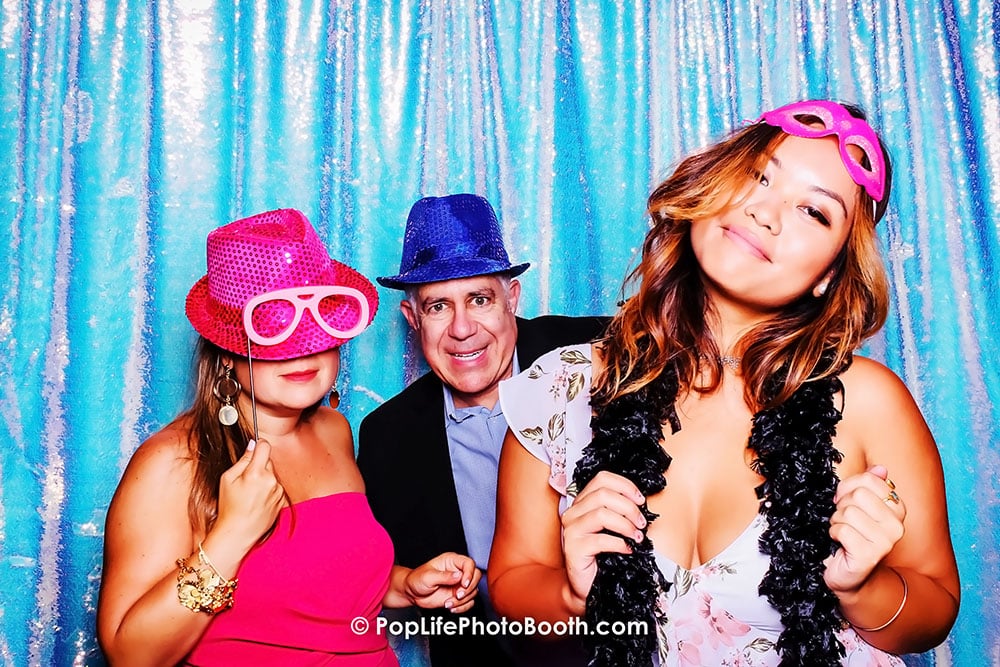 Cheerful group of three posing in a photo booth with colorful hats and accessories, capturing fun wedding memories.