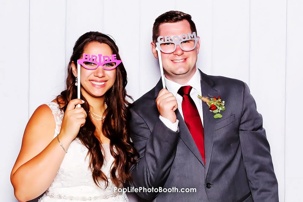 Bride and groom posing playfully with props at a wedding photo booth, showcasing joyful celebration and fun moments.