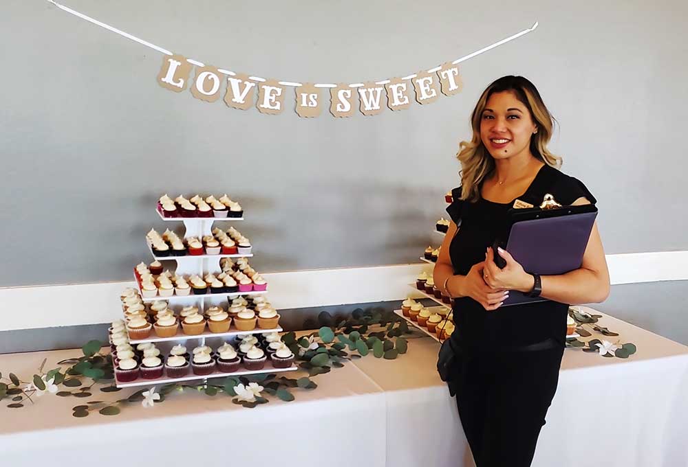Tiffany Foronda, event planner, standing beside a cupcake display with a "LOVE IS SWEET" banner, emphasizing event planning and celebration safety.
